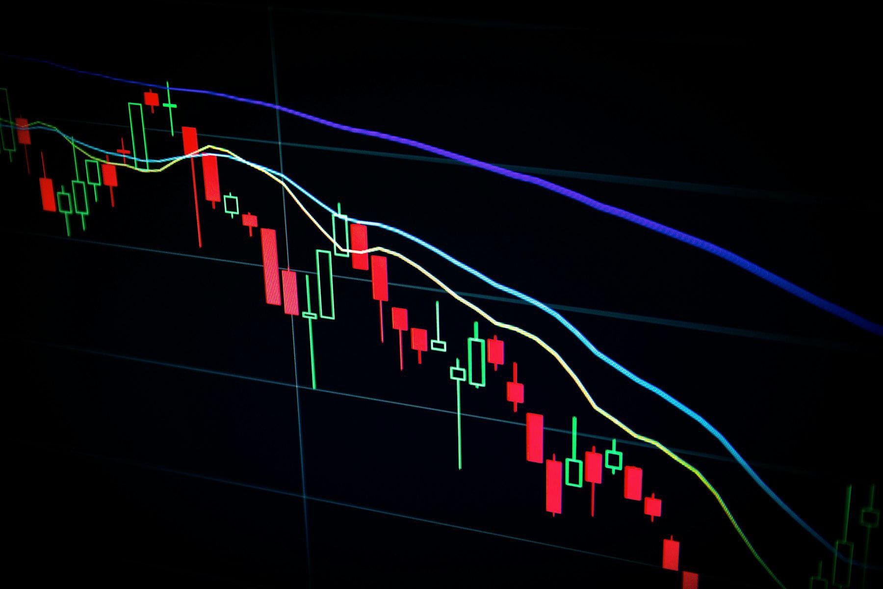 A candlestick trading chart on a dark screen showing a downward market trend